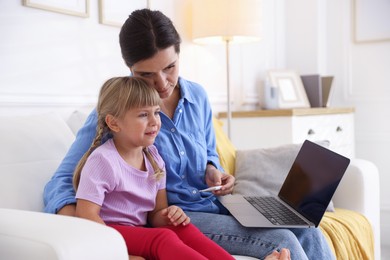 Photo of Telehealth. Mother and her sick daughter having online consultation with doctor via laptop on sofa at home