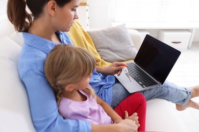 Photo of Telehealth. Mother and her sick daughter having online consultation with doctor via laptop on sofa at home