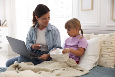 Photo of Telehealth. Mother and her sick daughter having online consultation with doctor via laptop on bed at home