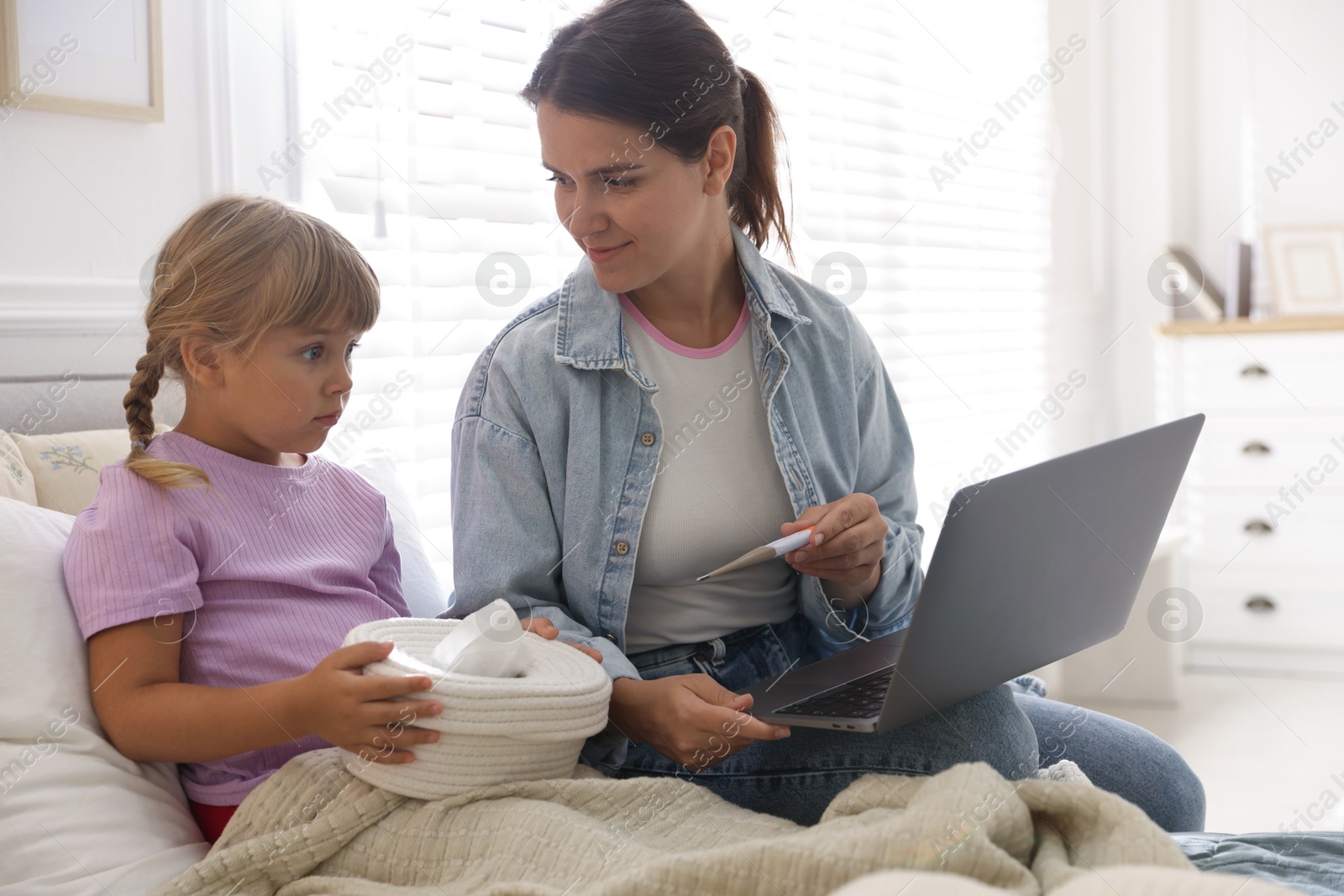 Photo of Telehealth. Mother and her sick daughter having online consultation with doctor via laptop on bed at home