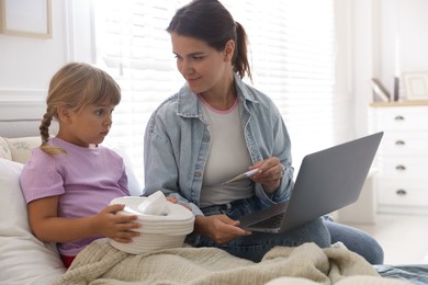 Photo of Telehealth. Mother and her sick daughter having online consultation with doctor via laptop on bed at home