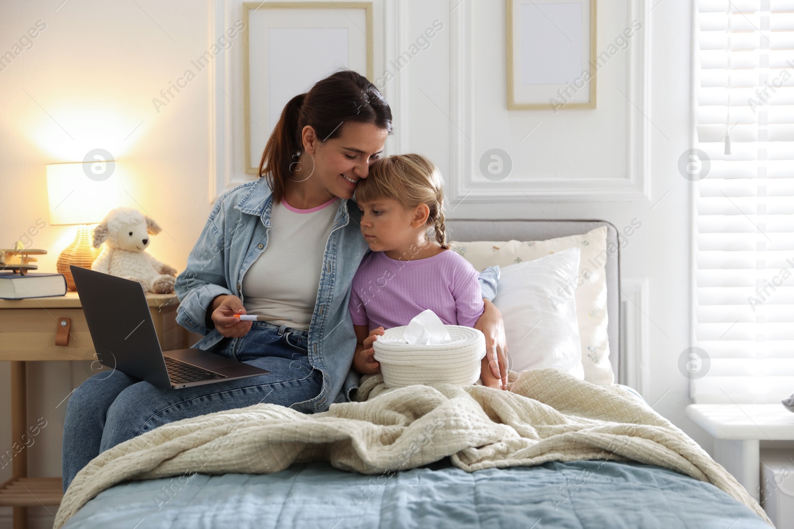 Photo of Telehealth. Mother and her sick daughter having online consultation with doctor via laptop on bed at home
