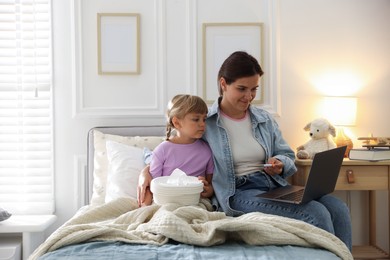 Photo of Telehealth. Mother and her sick daughter having online consultation with doctor via laptop on bed at home
