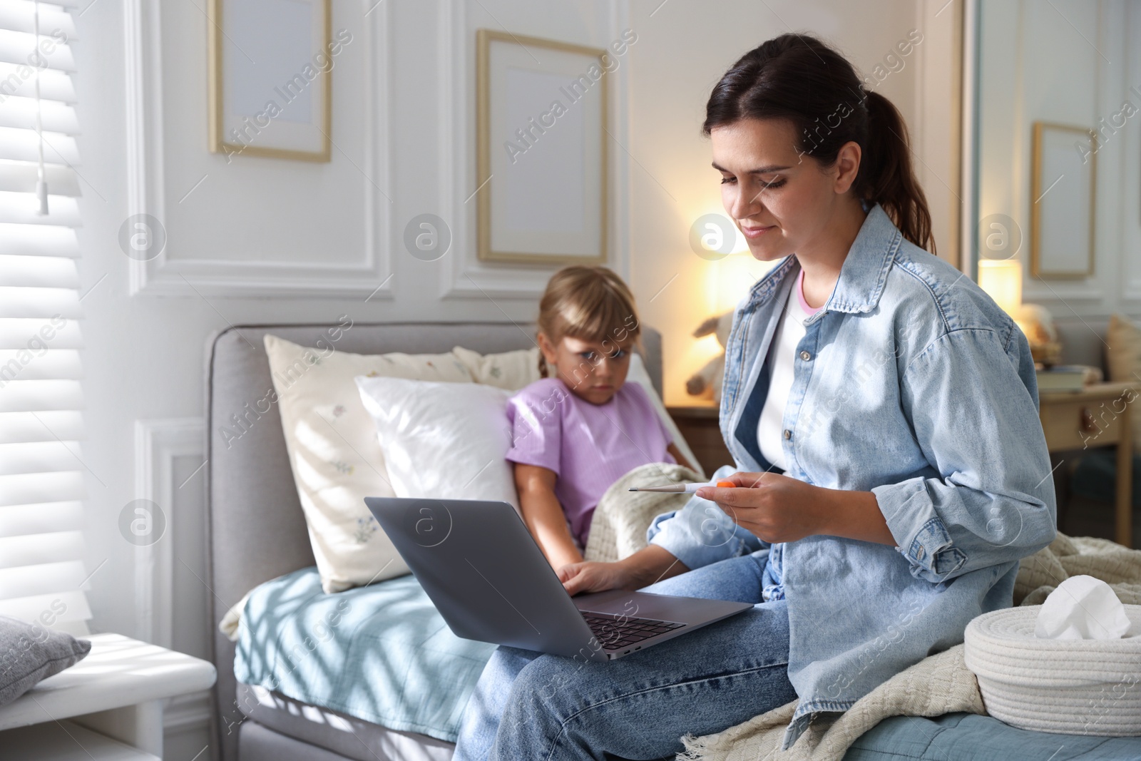 Photo of Telehealth. Mother and her sick daughter having online consultation with doctor via laptop on bed at home, selective focus