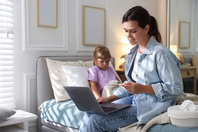 Photo of Telehealth. Mother and her sick daughter having online consultation with doctor via laptop on bed at home, selective focus