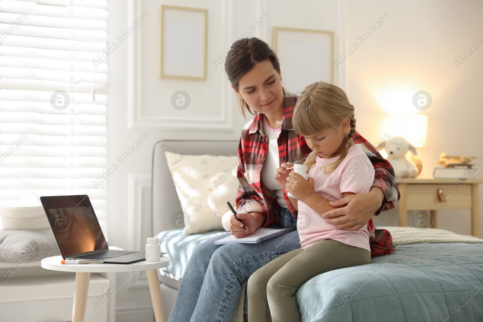 Photo of Telehealth. Mother and her daughter having online consultation with doctor via laptop on bed at home