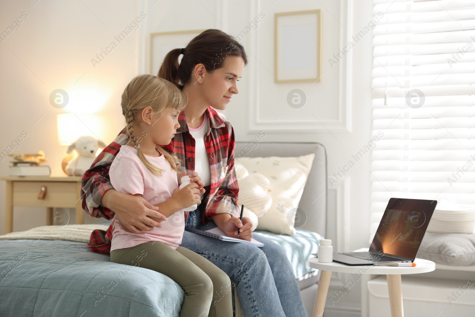 Photo of Telehealth. Mother and her daughter having online consultation with doctor via laptop on bed at home