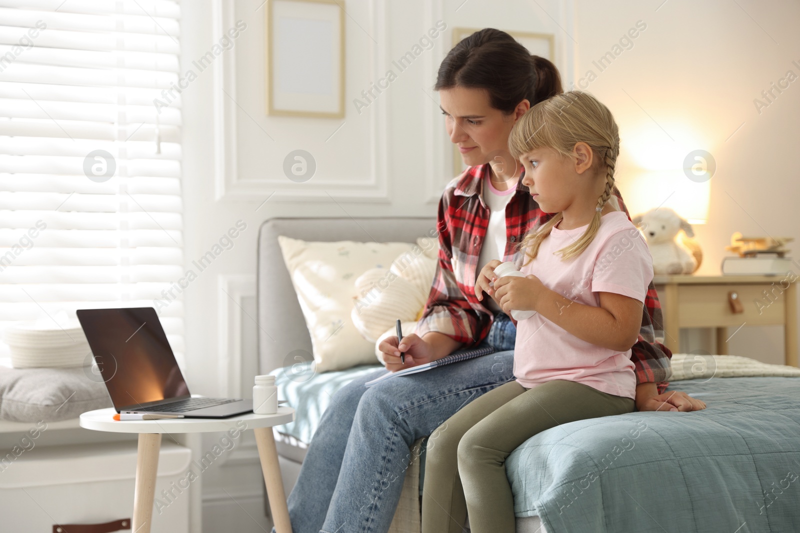 Photo of Telehealth. Mother and her daughter having online consultation with doctor via laptop on bed at home