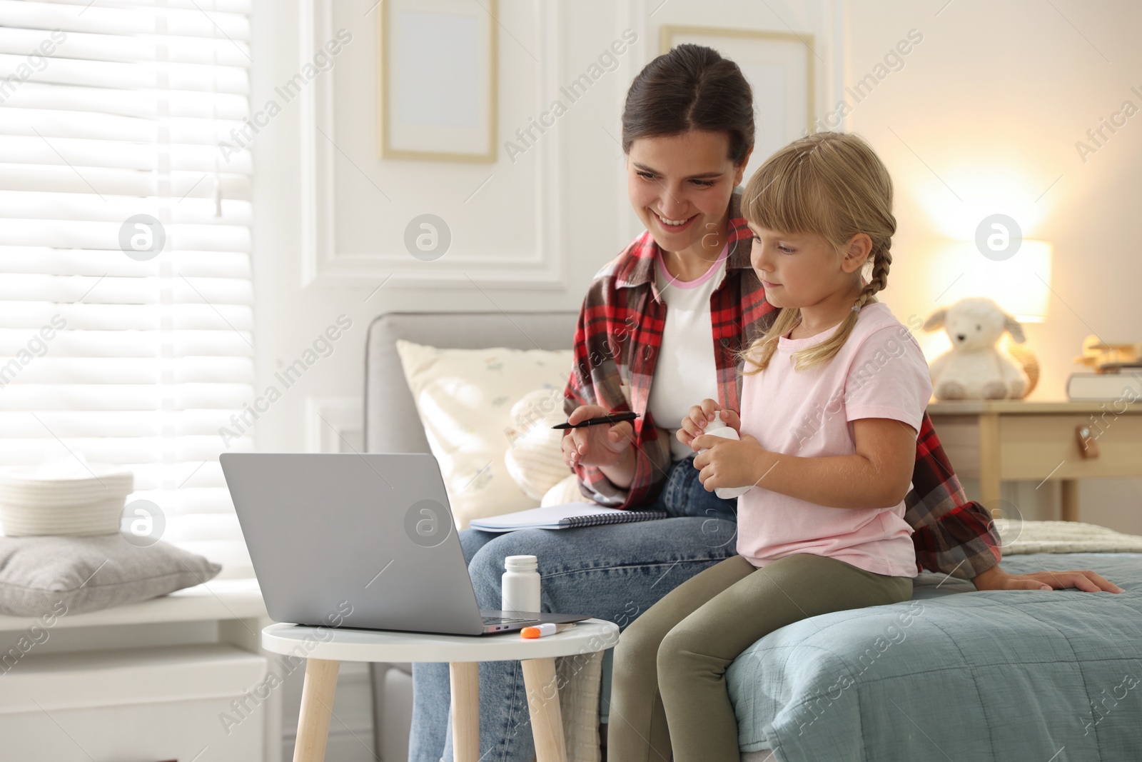 Photo of Telehealth. Mother and her daughter having online consultation with doctor via laptop on bed at home