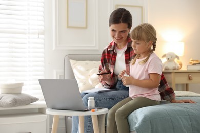 Photo of Telehealth. Mother and her daughter having online consultation with doctor via laptop on bed at home