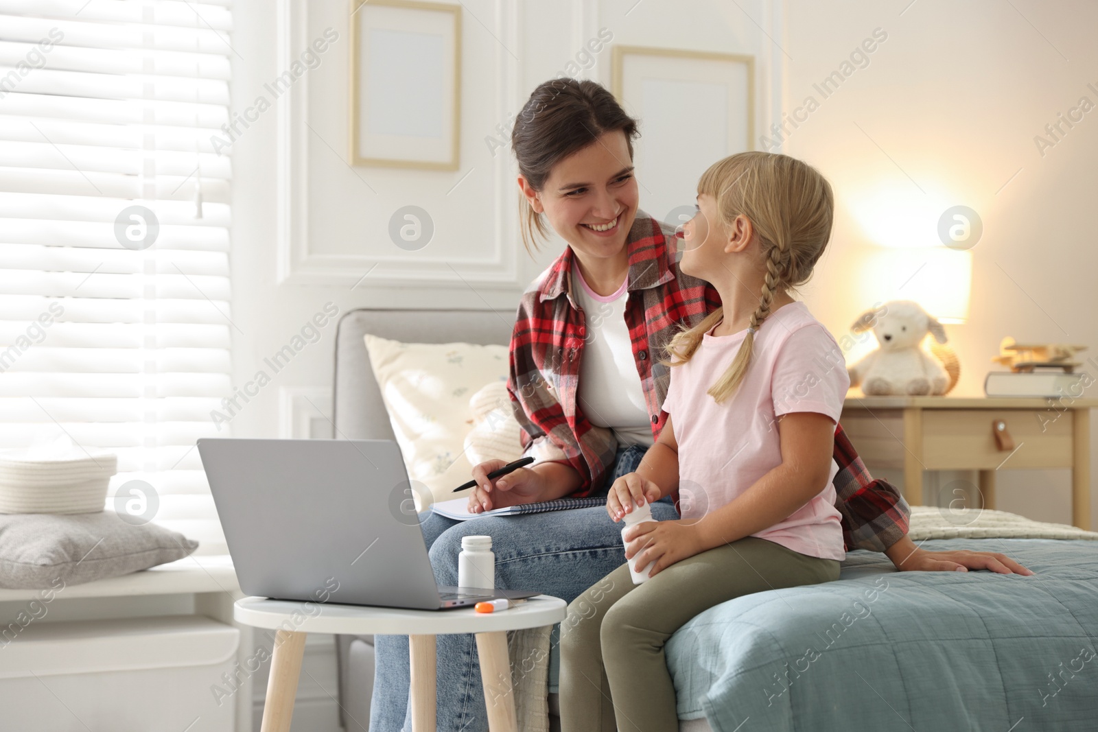 Photo of Telehealth. Mother and her daughter having online consultation with doctor via laptop on bed at home