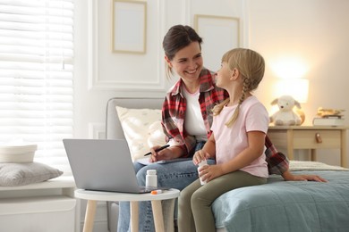 Photo of Telehealth. Mother and her daughter having online consultation with doctor via laptop on bed at home