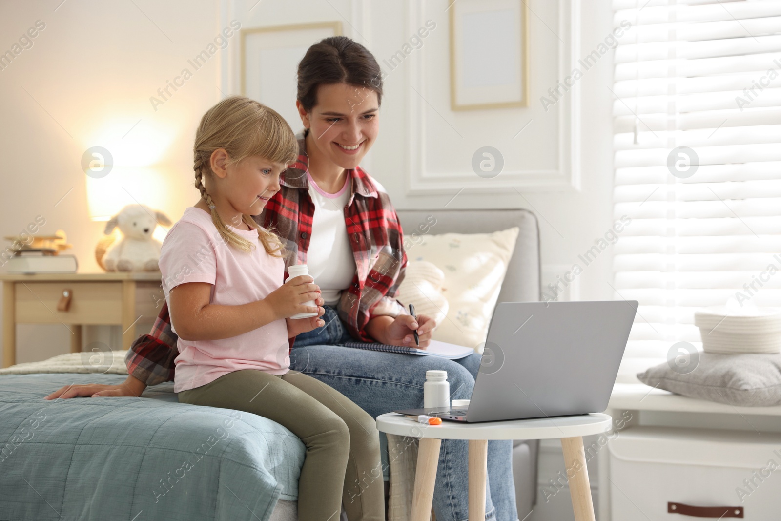 Photo of Telehealth. Mother and her daughter having online consultation with doctor via laptop on bed at home