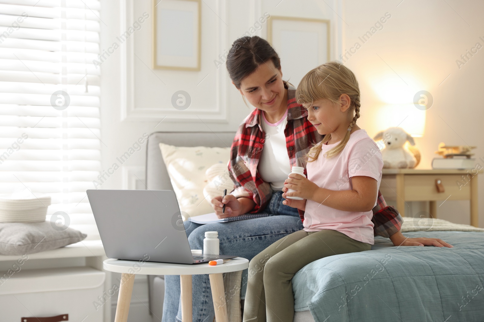 Photo of Telehealth. Mother and her daughter having online consultation with doctor via laptop on bed at home