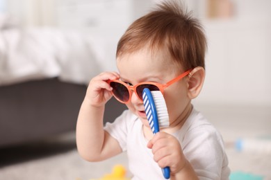 Photo of Cute baby with sunglasses and hair brush at home