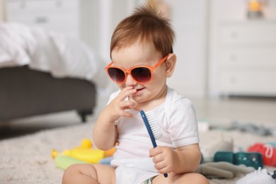 Photo of Cute baby with sunglasses and hair brush at home