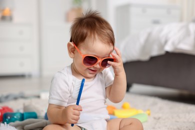Photo of Cute baby with sunglasses and hair brush at home