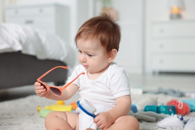Photo of Cute baby with sunglasses and hair brush at home