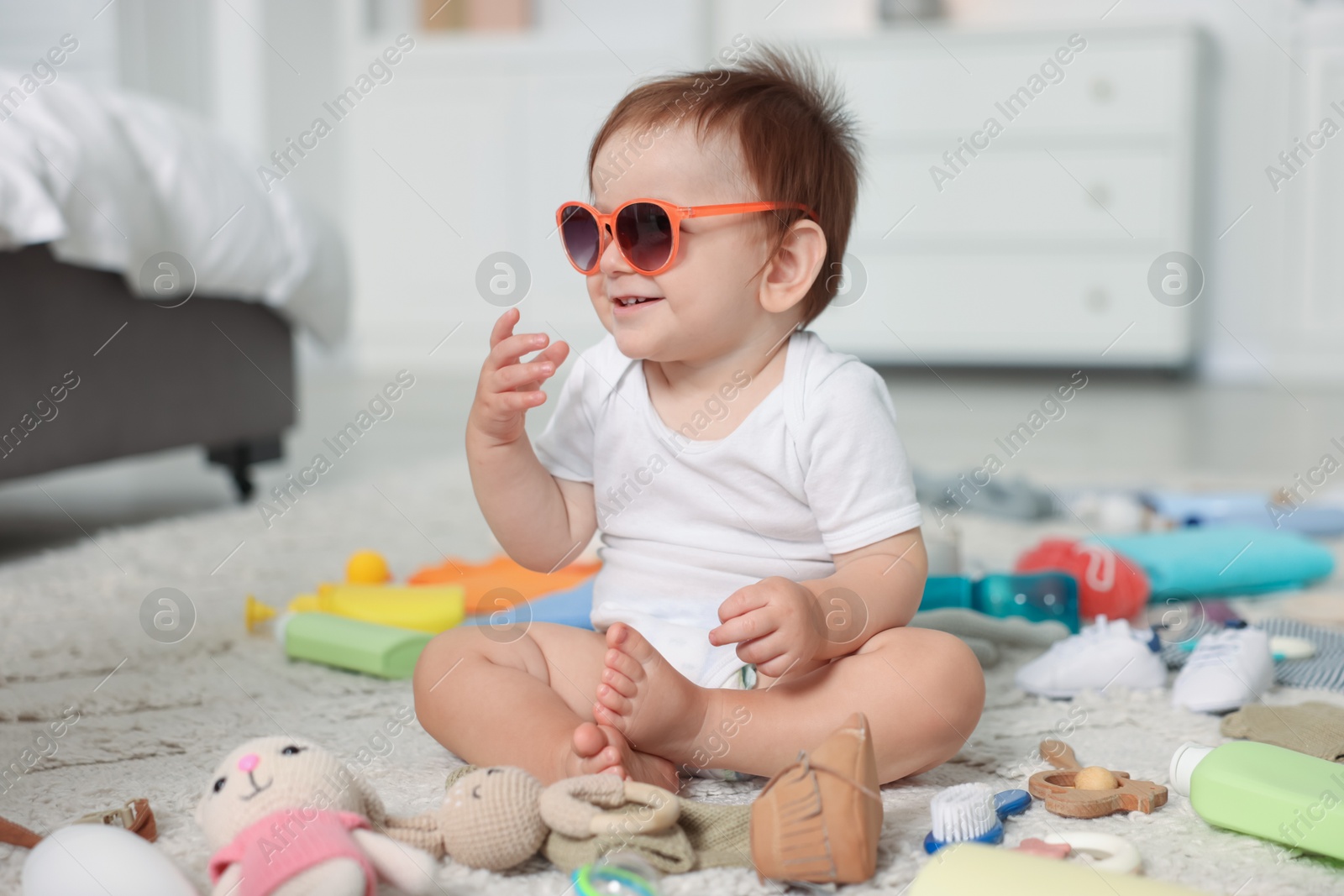 Photo of Cute baby with sunglasses and different accessories on floor at home