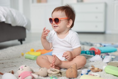 Photo of Cute baby with sunglasses and different accessories on floor at home