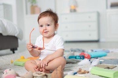 Photo of Cute baby with sunglasses and different accessories on floor at home
