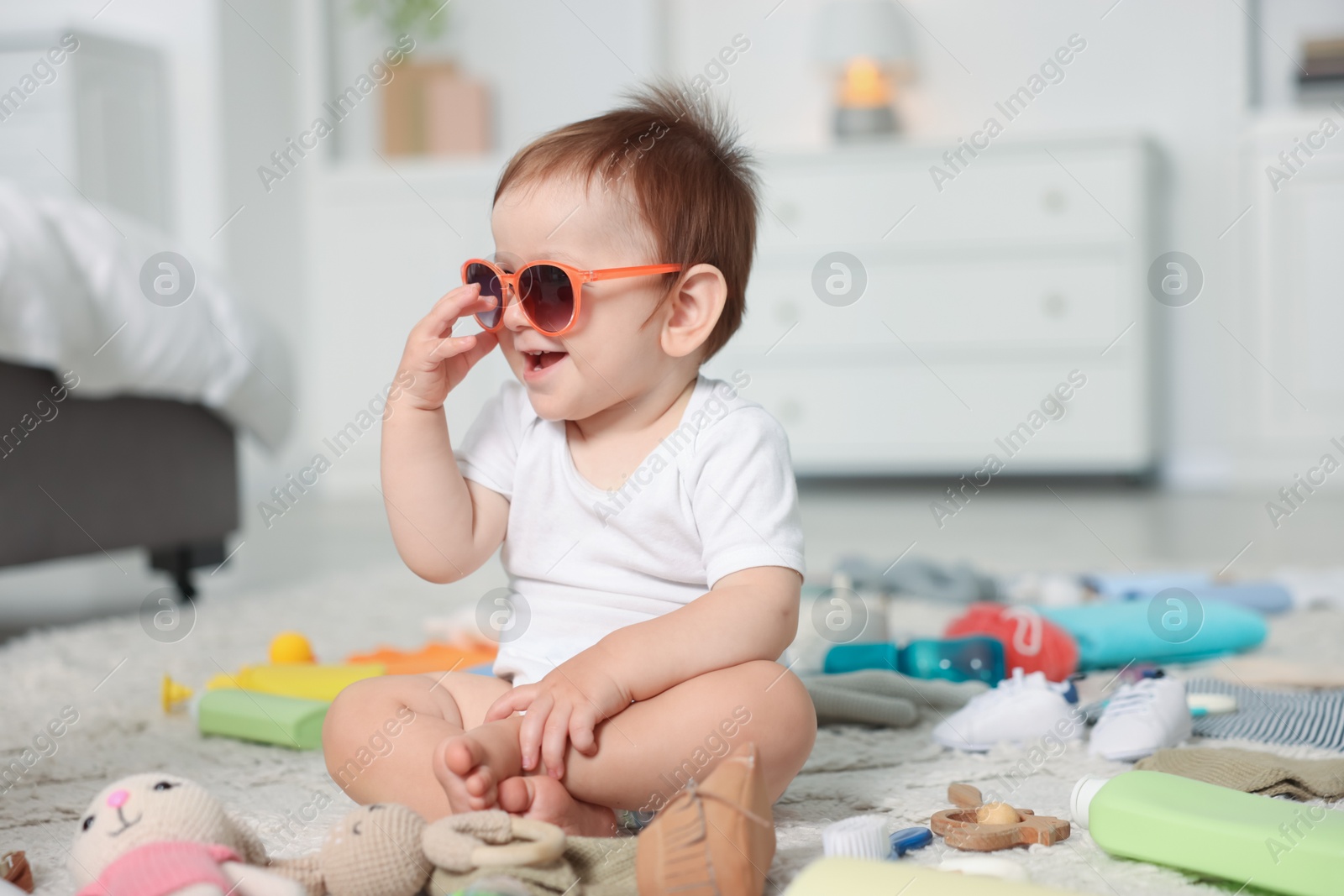 Photo of Cute baby with sunglasses and different accessories on floor at home