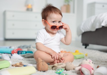 Photo of Cute baby with sunglasses and different accessories on floor at home