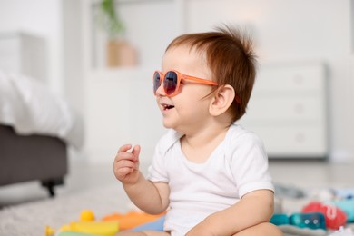 Photo of Cute baby with sunglasses on floor at home