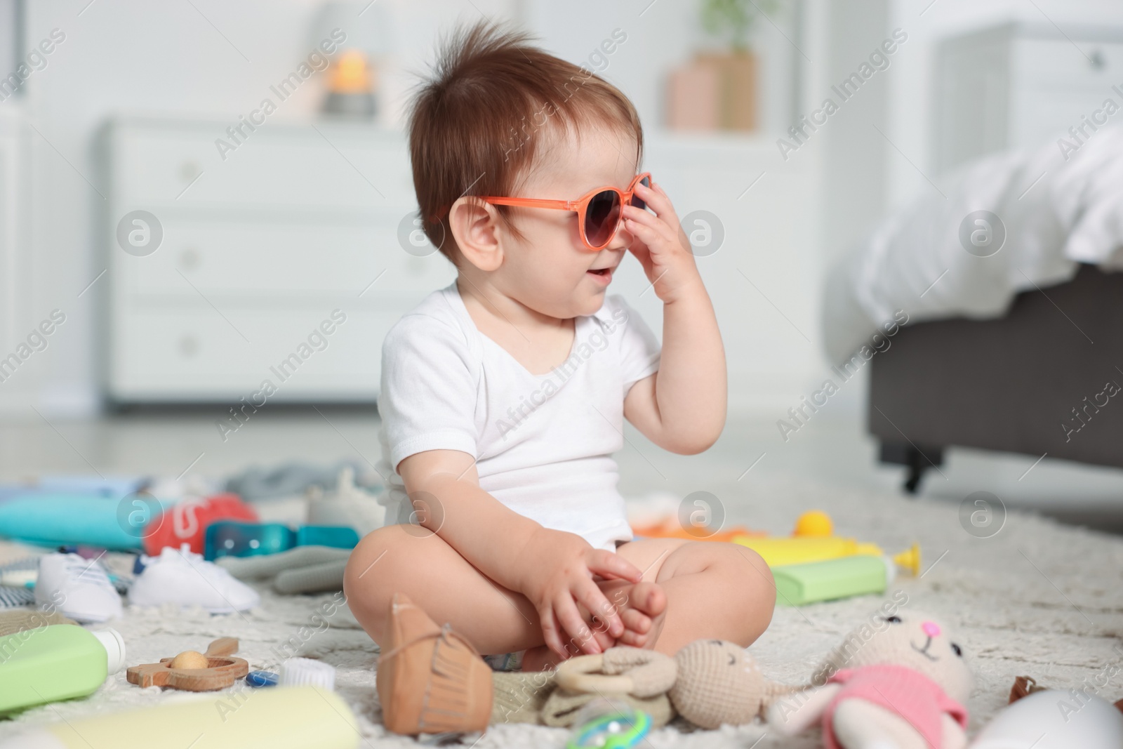 Photo of Cute baby with sunglasses and different accessories on floor at home