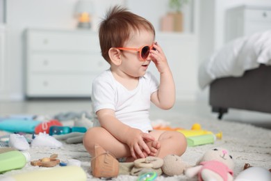 Photo of Cute baby with sunglasses and different accessories on floor at home