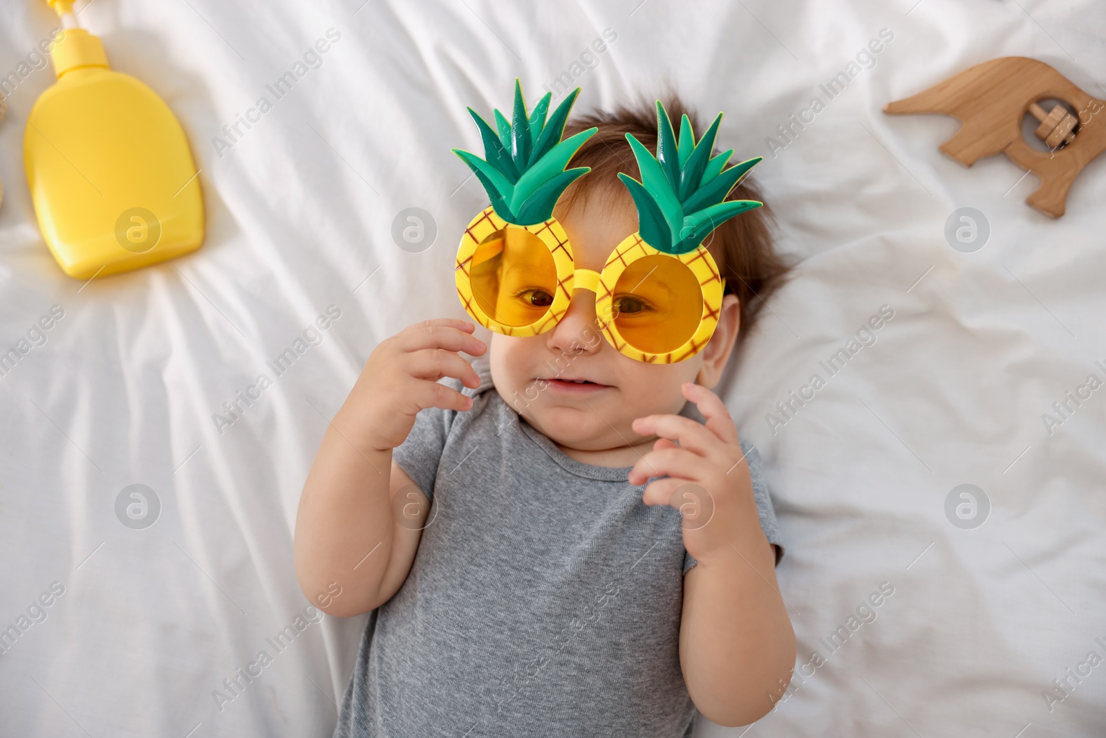 Photo of Cute baby with funny sunglasses and accessories on bed, top view