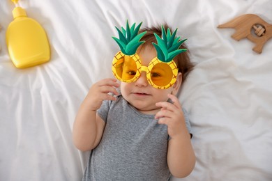 Photo of Cute baby with funny sunglasses and accessories on bed, top view