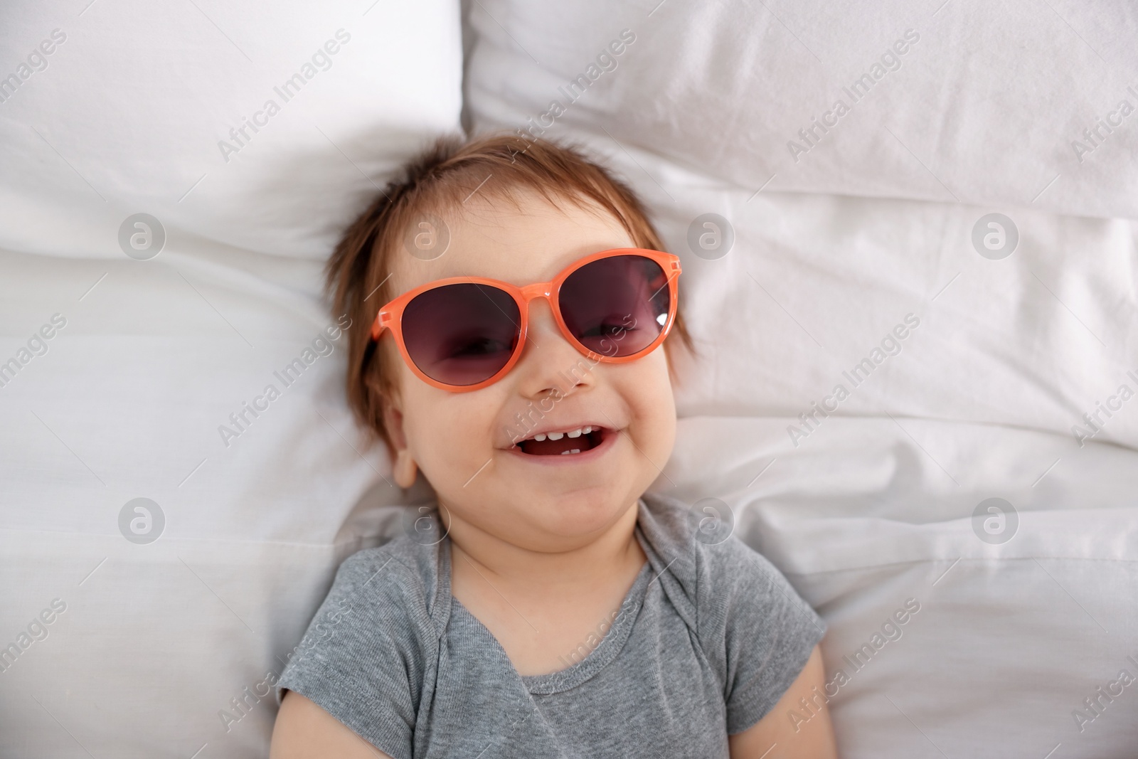 Photo of Funny baby with sunglasses lying on bed, top view