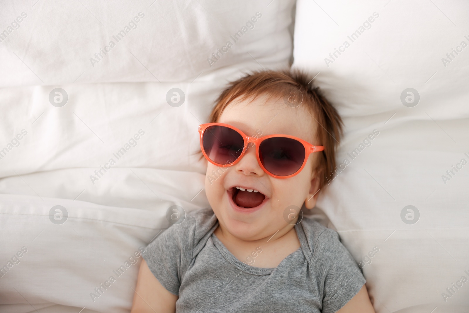 Photo of Funny baby with sunglasses lying on bed, top view