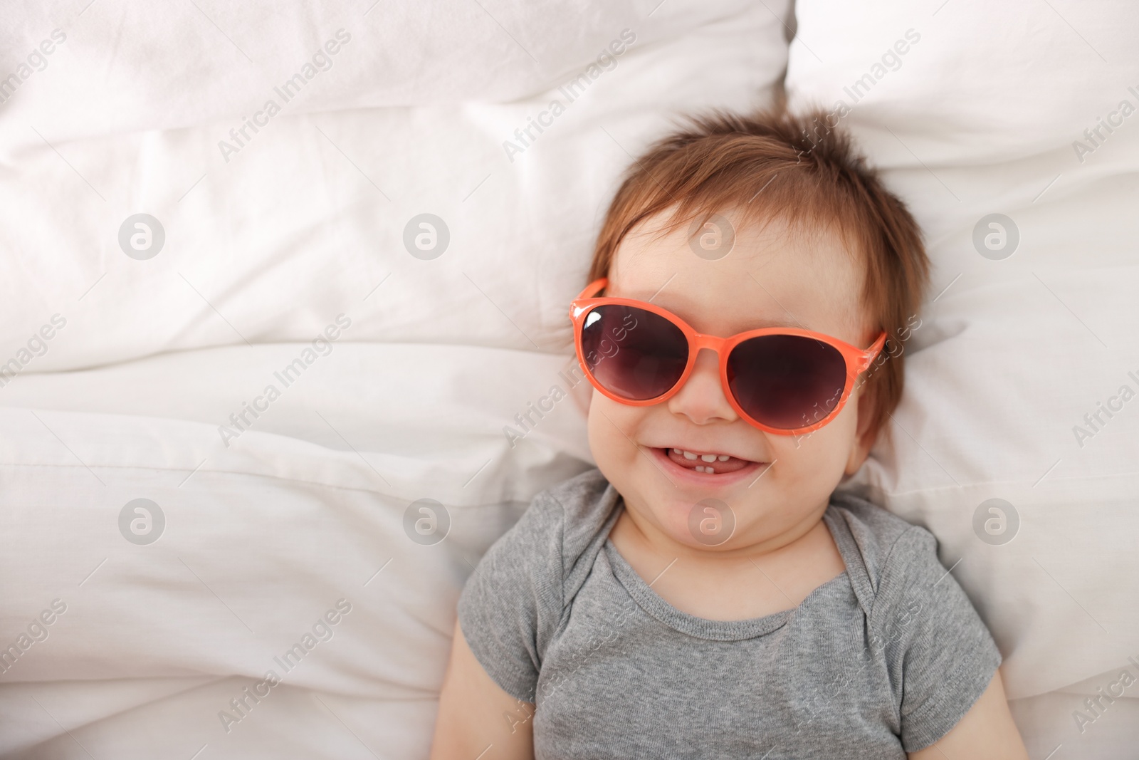 Photo of Funny baby with sunglasses lying on bed, top view