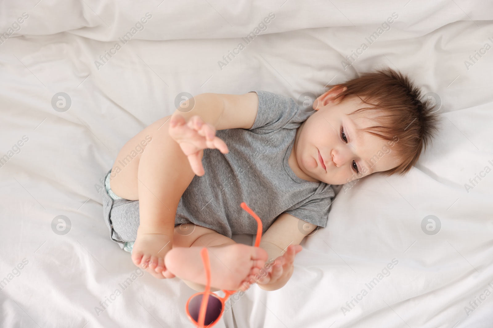 Photo of Funny baby with sunglasses lying on bed