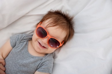 Photo of Funny baby with sunglasses lying on bed