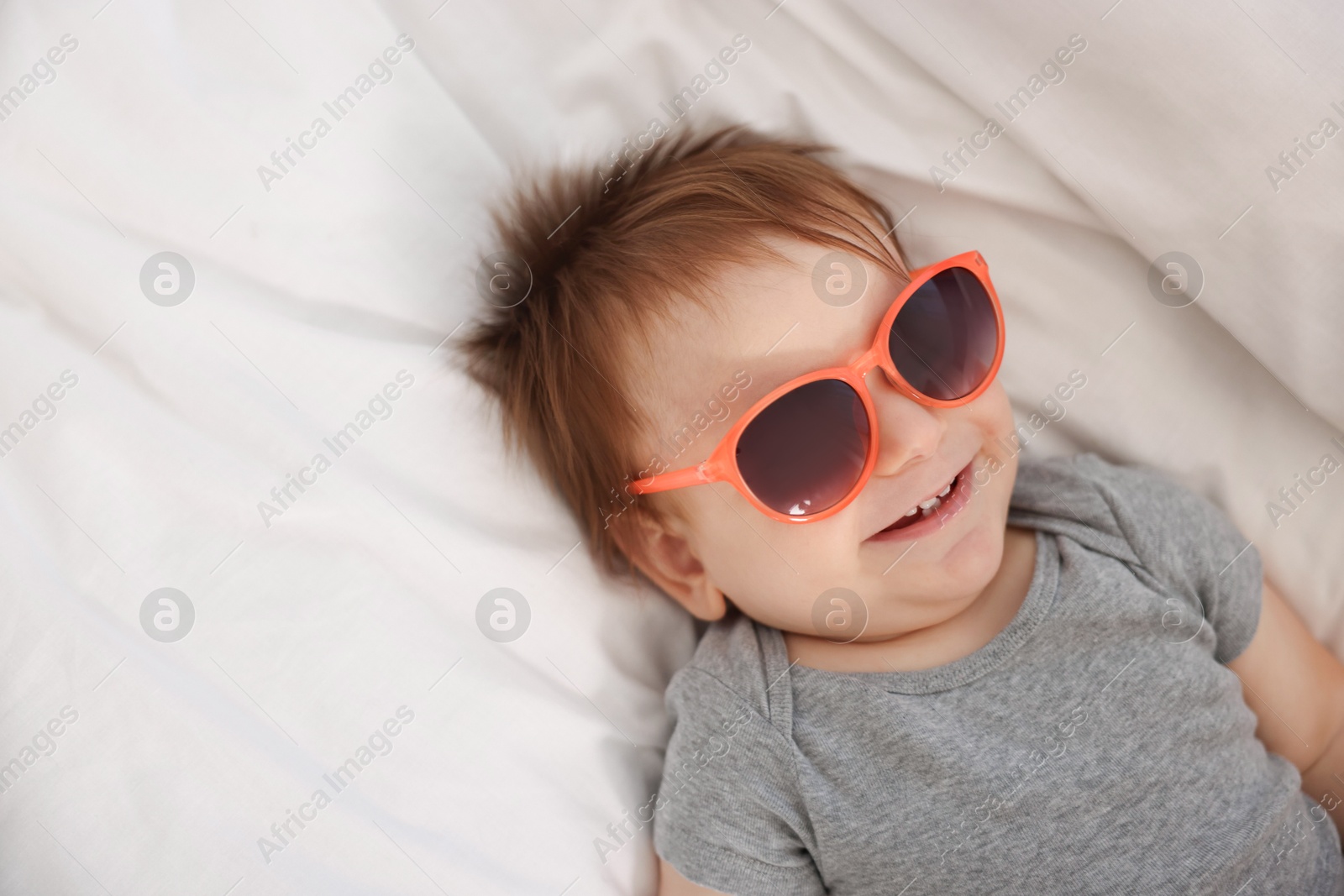 Photo of Funny baby with sunglasses lying on bed