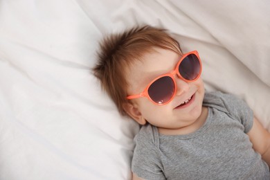 Photo of Funny baby with sunglasses lying on bed
