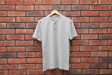 Photo of Hanger with gray t-shirt against red brick wall. Mockup for design