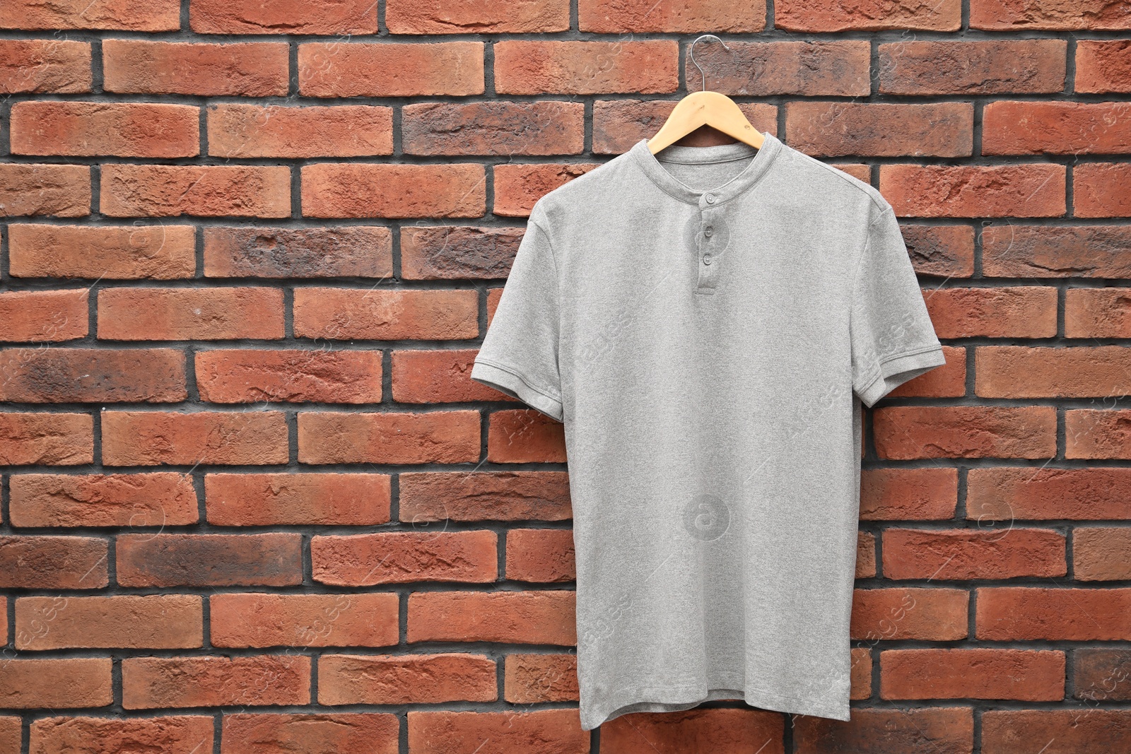 Photo of Hanger with gray t-shirt against red brick wall. Mockup for design