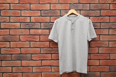 Photo of Hanger with gray t-shirt against red brick wall. Mockup for design