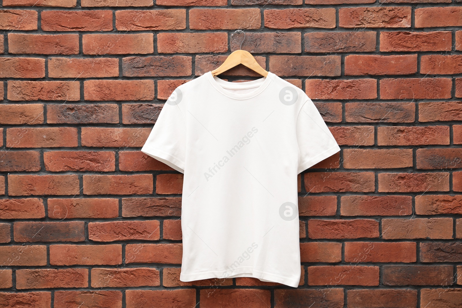 Photo of Hanger with white t-shirt against red brick wall. Mockup for design