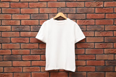 Photo of Hanger with white t-shirt against red brick wall. Mockup for design