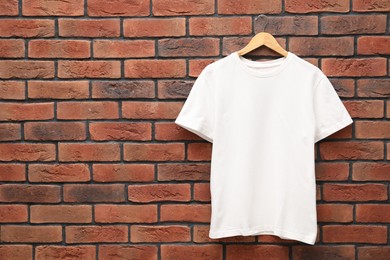 Photo of Hanger with white t-shirt against red brick wall. Mockup for design