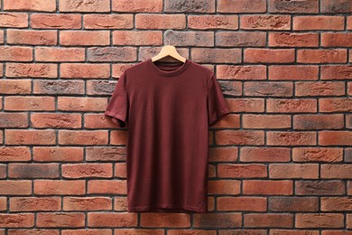 Photo of Hanger with brown t-shirt against red brick wall. Mockup for design