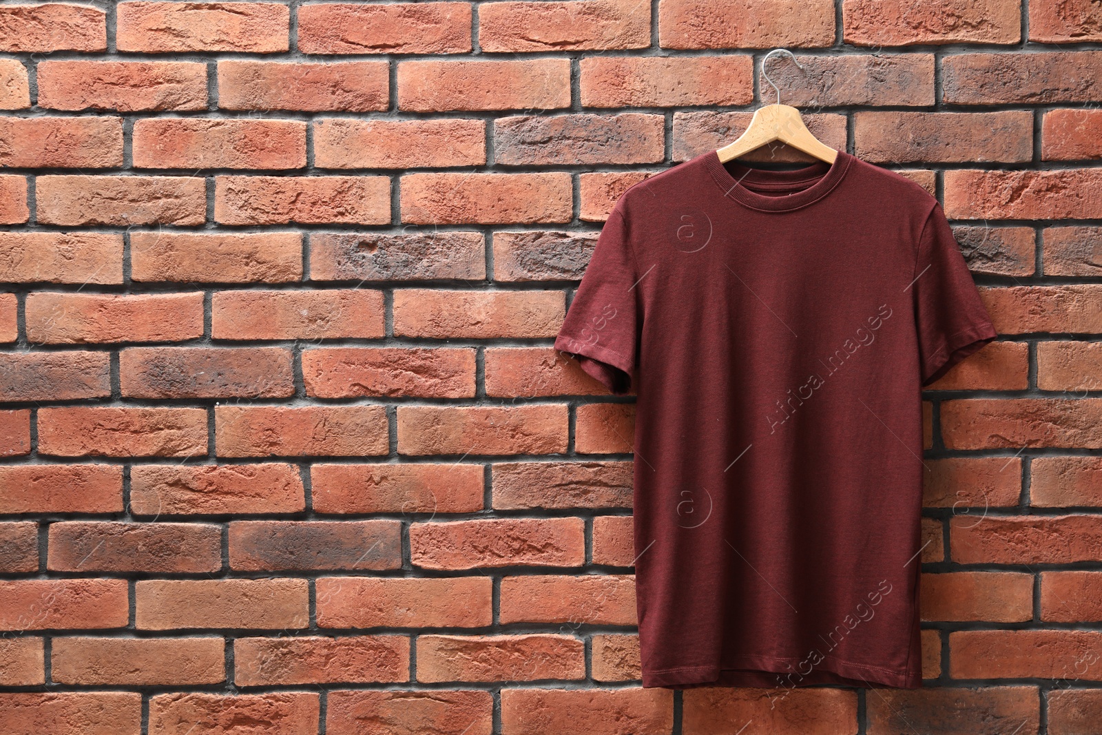 Photo of Hanger with brown t-shirt against red brick wall. Mockup for design