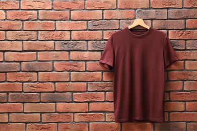 Photo of Hanger with brown t-shirt against red brick wall. Mockup for design