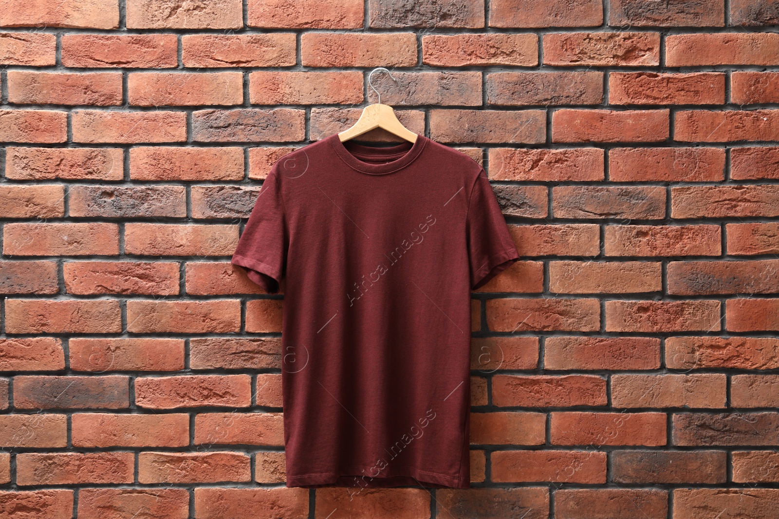 Photo of Hanger with brown t-shirt against red brick wall. Mockup for design