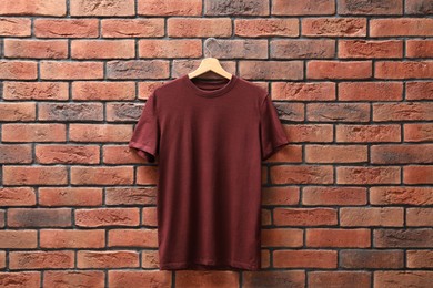 Photo of Hanger with brown t-shirt against red brick wall. Mockup for design